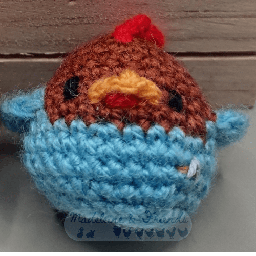 Close up of a small crochet chicken, showing a closer look at the eyes, beak and wattle.