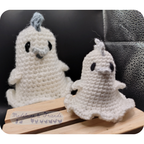 Two crochet ghost chickens in the style of bed sheet ghosts. Their bodies are completely white. They have grey combs, beaks and wattles, and black eyes. One is three times the size of the other.