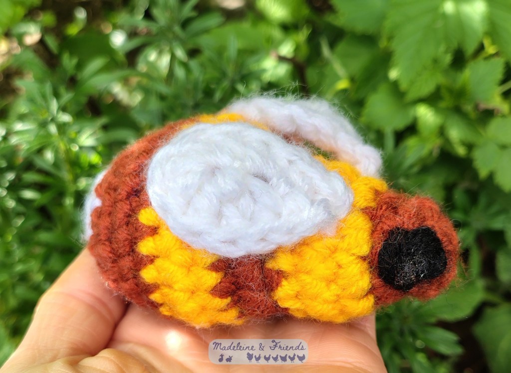 A large yellow and brown crochet bee sitting on the palm of someone's hand.